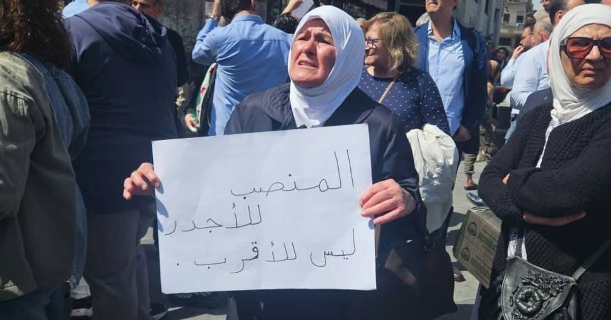سيدة مسنة في تحمل لوحة كتب عليها "المنصب للأجدر وليس للأقرب"