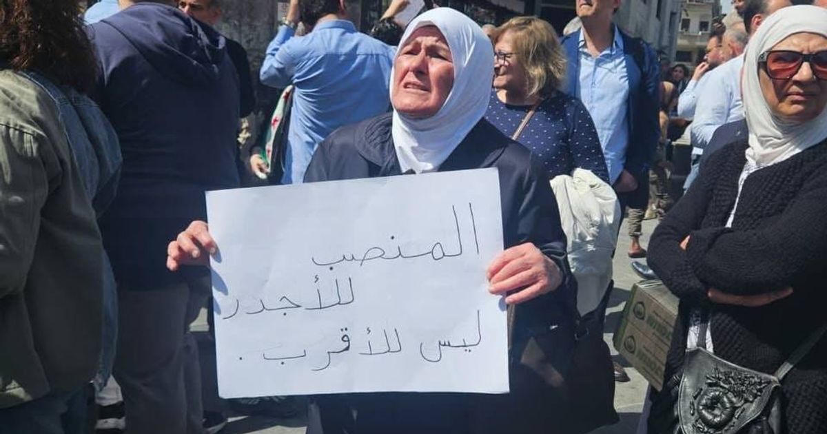 سيدة مسنة في تحمل لوحة كتب عليها "المنصب للأجدر وليس للأقرب"